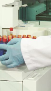 Gıcır gıcır beyaz laboratuar önlüğü ve mavi lateks eldivenlerle donanmış kendini adamış genç bir laboratuvar teknisyeni şık, modern bir laboratuvar masasındaki her test tüpünü titizlikle inceliyor. Bu temel hazırlık eylemi kesinliği garanti eder.