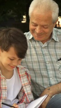 Küçük, hoş bir beyaz çocuk dikkatle defterine yazarak dedesinin değerli bilgeliğini yakalıyor. Parktaki bankta sıcak güneş ışığında yıkanan gri saçlı emekliler gururla ışıldıyor. Dokunaklı bir bağ anı yaratıyor.