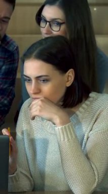 Hem erkek hem de kadın öğrencilerden oluşan çeşitli bir grup, gösterişli, modern bir konferans salonunda dizüstü bilgisayar üzerinde derin bir işbirliği içinde. İfadeleri, sıcak ahşap tonlar ve yumuşak ışıklandırma ile çevrili merak ve takım çalışması yayar.