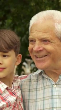 Güneşten sırılsıklam olmuş bir parkta, sevimli küçük bir çocuk büyükbabasıyla bir sırrı paylaşmak için öne eğiliyor ve dokunaklı bir bağ anı yaratıyor. Çekici esmer çocuk, neşeli bir şapkayla süslenmiş, yakışıklı büyükbabası gibi neşe saçıyor.