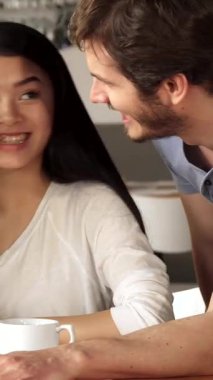 Canlı bir kafe ortamında, canlı, melez bir grup arkadaş bir akıllı telefon ekranından etkilenmiş, yüzleri neşeyle parlıyor. İki beyaz erkek, biri Afrikalı Amerikalı, biri Asyalı olmak üzere iki kızın önünde şakacı bir şekilde duruyorlar.