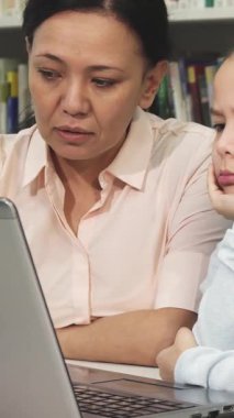 Canlı kitaplarla dolu samimi bir kütüphanede, yorgun küçük bir kız çenesini elinde dinlendirip dikkatle dizüstü bilgisayara bakıyor. Annesi, kaygı ve cesaret dolu bir bakışla, sabırla ona yardım ediyor, aşkın derin bağını vurguluyor ve