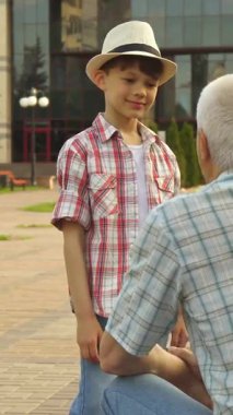 Keyifli bir Kafkas kıdemli adam neşeli bir parkta sevimli torunuyla coşkulu bir beşlik paylaşıyor, neşe saçıyor. Küçük çocuk, modaya uygun bir gömlek ve şık bir şapka giymiş, heyecan dolu ışınlar içinde, canlı bir yeşillik ve bir