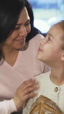 Olgun bir Asyalı kadın ve sevimli küçük kızı, ağız sulandırıcı hamur işleriyle dolu canlı bir fırının önünde coşkuyla başparmaklarını kaldırarak gülümsüyorlar. Bu hoş an, ailenin sıcaklığını özetliyor.