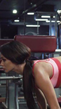 Gösterişli, uzun siyah saçlı, at kuyruklu, kendini işine adamış genç bir kadın şık, modern bir spor salonunda ağır bir halterle kendinden emin bir şekilde viraj alıyor. Enerjik atletik kıyafeti vücudunu vurguluyor. Kararlılık ve enerji saçıyor.