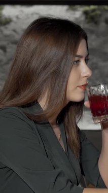 Şık bir restoran ortamında ferahlatıcı bir kokteyl içerken kameraya uzun, dalgalı saçları olan çekici genç bir kadın. Onun ışıl ışıl gülüşü ve zarif kıyafeti davetkar bir kutlama atmosferi yaratıyor ve sofistike, mükemmel bir...