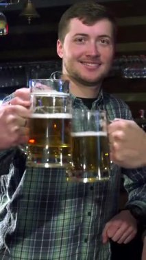 Üç neşeli arkadaş hareketli bir barda buzlu bira bardaklarını kaldırarak arkadaşlığın ve kutlamanın ruhunu somutlaştırıyorlar. Yakın çekim, onların neşeli gülümsemelerini ve modaya uygun kıyafetlerini yakalar, kahkahalarla dolu canlı bir atmosfer yaratır.