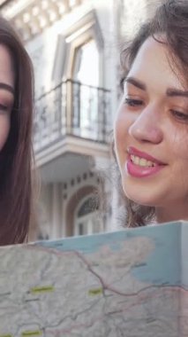 Canlı bir şehir ortamında, biri kıvırcık saçlı, diğeri düz bukleli iki genç kadın, ayrıntılı bir haritayı hevesle inceliyor, yüzleri heyecan ve merakla aydınlanıyor. Bu büyüleyici an maceranın heyecanını özetliyor.