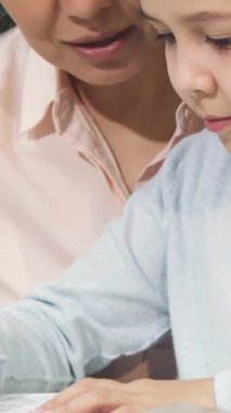 Bu yürek ısıtan yakın plan ev ödevine dalmış küçük bir kızı yakalar. Bu sırada sevgili annesi yanında gururla ışıldar. Konforlu ev ortamı, öğrenme sevincini ve besleyici bağları gözler önüne seriyor.