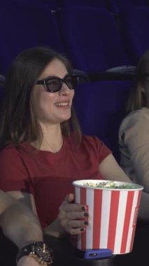 Üç boyutlu şık gözlüklerle süslenmiş iki neşeli çift, sinemanın ışıltısının tadını çıkarıyor, kahkahalarını ve büyük bir kova patlamış mısırlarını paylaşıyorlar. Canlandırıcı gülümsemeleri ve rahat duruşları davetkar bir atmosfer yaratıyor, keyifli bir gece için mükemmel.