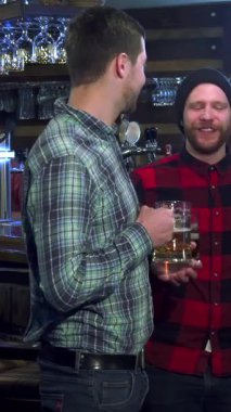 Neşeli üç beyaz adam neşeli bir barda kadehlerini kaldırarak arkadaşlığı kahkaha ve arkadaşlıkla kutluyorlar. Şapkalı şık sakallı adam neşeli bir atmosferle çevrili samimi bir tostu paylaşıyor.