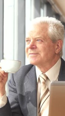 Keskin bir takım elbise ve kravat takmış seçkin bir Kafkas işadamı kafenin penceresinden dışarı dikkatlice bakarken kahvesini yudumluyor. Yanında dizüstü bilgisayarı açıkken, sakin bir şehirle çevrili modern profesyonellik ve sükuneti somutlaştırıyor.