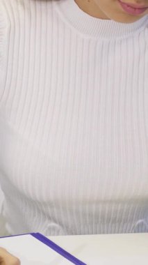 Bu yakın plan çekimde zarif beyaz kazaklı kararlı bir genç kadın şık ofis masasında dokümanları dolduruyor. Işıl ışıl gülüşü ve odaklanmış ifadesi profesyonellik ve yaratıcılık yayıyor.