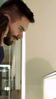 Lüks bir butikte nefes kesen mücevher gösterisine hayran olan modaya uygun beyaz bir çift, gözleri zevkle parıldıyor. Sakallı adam ve zarif kız arkadaşı, zarif yüzükleri keşfederek neşeli bir gülümseme sergiliyorlar.