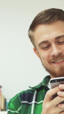 Şık sakallı ve bıyıklı neşeli bir genç adam, parlak, davetkar bir kütüphanede telefonunda mesaj okurken kahkahaya boğuluyor. Etrafı renkli kitaplıklarla çevrili sıcak gülüşü, öğrenci hayatının neşesini yansıtıyor.