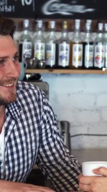 Büyüleyici bir kafede şık bir tişörtü olan genç bir erkek barmen, sarışın bir kadınla kahvesini yudumlarken hararetli bir sohbet eder. Dostça etkileşimleri sıcak ve davetkar bir atmosfer yaratıyor. Sosyalleşmek ve zevk almak için mükemmel.