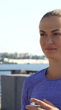 Nehir kenarında ışıl ışıl genç bir kadın baş parmağını kaldırırken neşeyle şişesinden su yudumluyor. Parlak gülüşü, köprülerin ve renkli binaların yer aldığı çarpıcı şehir manzarasıyla birleşince canlandırıcı bir atmosfer yaratıyor.