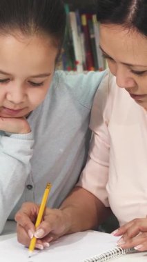 Neşeli bir Asyalı anne, parlak küçük kızına ev ödevlerinde rehberlik eder, rahat ve davetkar bir öğrenme ortamı yaratır. Gülümsemeleri ve yakın etkileşimleri, aile bağlarının güzelliğini ve neşesini gösteren sıcaklığı yayıyor.
