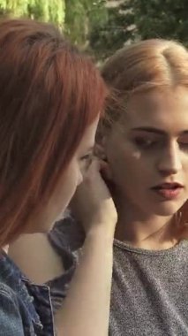 Sakin bir park ortamında, sarışın bir kız özenli kızıl saçlı arkadaşıyla en derin düşüncelerini paylaşıyor. İkisi de yemyeşil ve çiçek açan kırsal bir bankta oturuyor. Sıcak yaz ışığı yumuşak bir parıltı yayar,