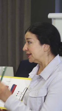 Dinamik kıdemli bir iş kadını, canlı iş diyagramlarını nişanlı meslektaşlarına gösteren bir tartışmayı tutkuyla yönetiyor. Kendine güveni ve rengarenk çizelgeleri işbirliği ve yenilik için ilham verici bir atmosfer yaratıyor.