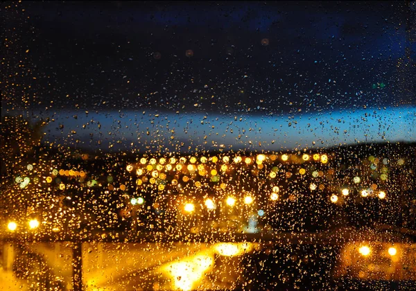 在雷雨后 玻璃和夜间城市灯光上的雨滴模糊背景 图库图片