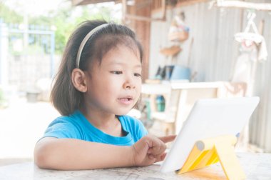 Asyalı Kız çevrimiçi kurs öğreniyor veya evde dijital kablosuz aygıt veya tablet üzerinden oyun oynuyor Teknoloji e-öğrenme kavramı olarak.