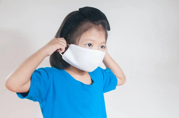 Asian child Girl or kids in blue Shirt wearing cloth mask to protect Covid 19 virus infection as medical safety prevention concept against white background.