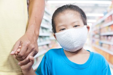 Tıbbi koruyucu maske takan küçük Asyalı kızlar babalarının elini halka açık bir alışveriş merkezinde ya da havaalanında tutuyor.