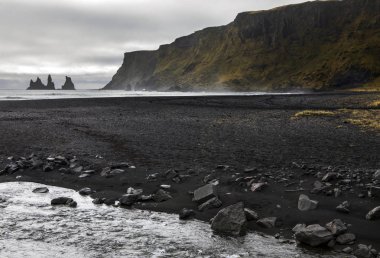 Siyah kum ve Reynisdrangar, Bazalt deniz yığınları üzerinde İzlanda'nın Güney kıyılarında Vik balıkçı köyü yakınındaki bir görünüm.