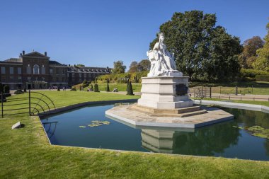 Londra, İngiltere - 27th Eylül 2018: Kensington Gardens Londra'da Kraliçe Victoria taç giyme elbisesi 1837 yılında tasvir eden bir heykel. Kensington Sarayı arka planda olduğunu.