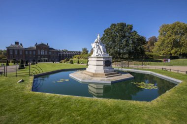 Londra, İngiltere - 27th Eylül 2018: Kensington Gardens Londra'da Kraliçe Victoria taç giyme elbisesi 1837 yılında tasvir eden bir heykel. Kensington Sarayı arka planda olduğunu.