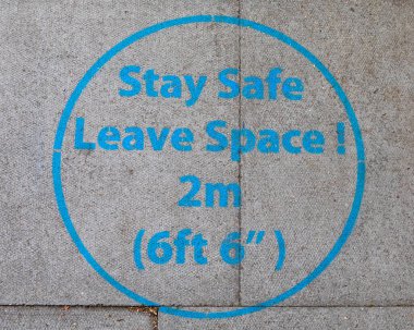 Londra, İngiltere 'de kaldırımda bir tabela, yayalara güvenli kalmalarını ve diğer insanlardan 2 metre uzakta tutarak sosyal mesafeye uymalarını söylüyor..