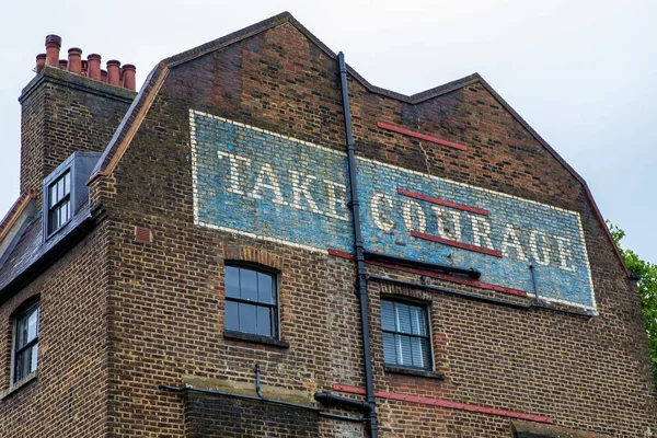 Looking up at the vintage Take Courage ghost sign, located on Redcross Street in London, UK.
