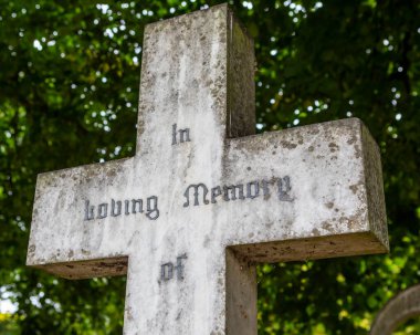 In Loving Memory of inscribed on a stone cross in a graveyard or cemetery. clipart