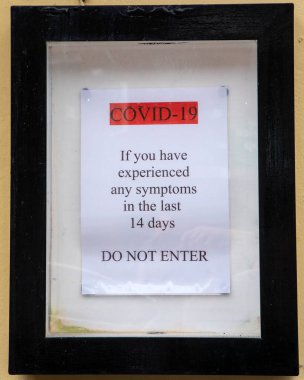 Dorset, İngiltere 'deki bir dükkânın girişinde Coronavirus belirtileri gösteren potansiyel ziyaretçilere girmemelerini söyleyen bir tabela..