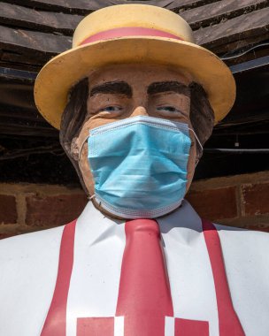 Geleneksel ve ikonik Kasap heykeli Coronavirus salgını sırasında maske takarak İngiltere 'de bir kasap dükkanının önünde duruyor..