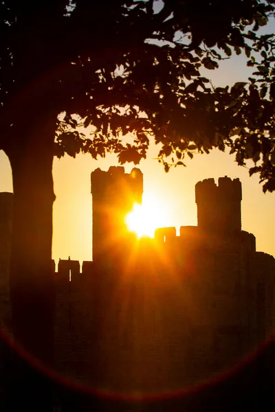 A silhouetted view of the historic Caernarfon Castle at sunset, in the town of Caernarfon in North Wales, UK.