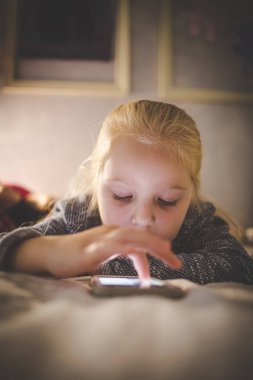 Bir akıllı telefon video izleme onun yatağında döşeme güzel sarışın bebek kız