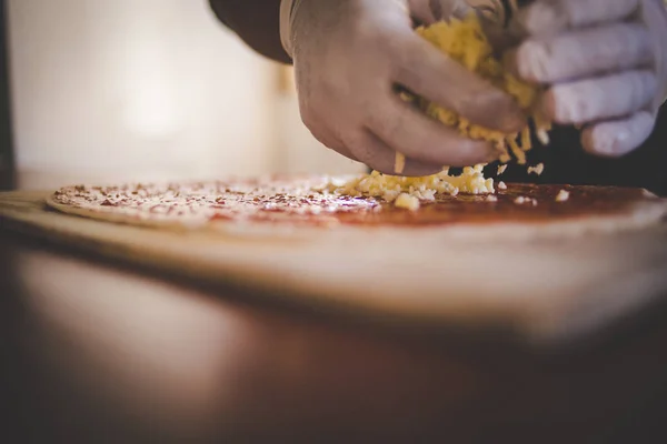 Close up image of a cook adding toppings and cheese to a gourmet wood fired pizza