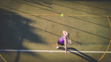 Yükü bir dron ile gelen genç bir kadın tenis kortunda tenis oynamaya havadan görüntü vurdu