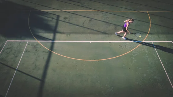 一个年轻女子在网球场上打网球的空中图像从头顶上的无人机拍摄 — 图库照片