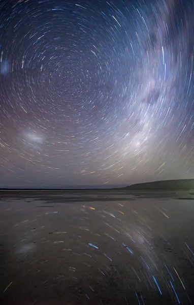 Startrail image over a salt pan at night with the reflection of the startrail in the water