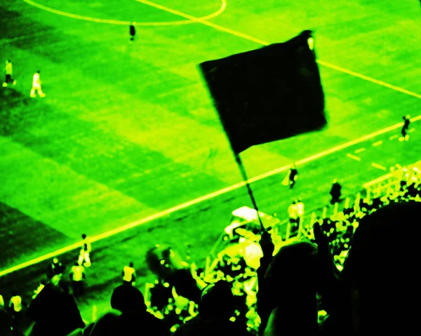 Fußballfans bejubeln im Stadion das Tor ihrer Mannschaft mit Fahnen, Transparenten und Schals. Gelbgetönte Sicht lizenzfreie Stockfotos