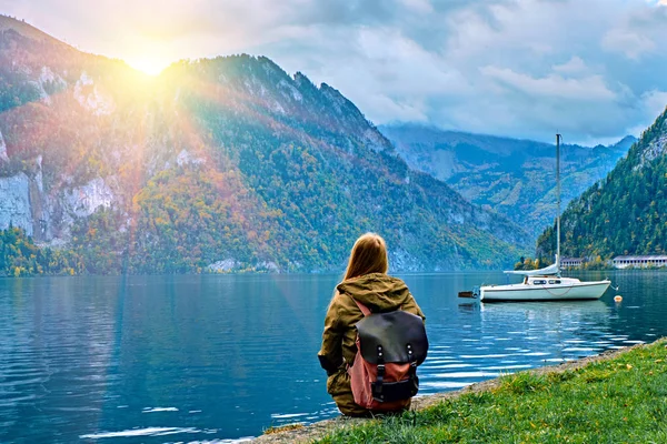 Joven turista con mochila mirando el hermoso amanecer panorámico en el lago de los Alpes austríacos. Hipster vacaciones de viaje en los Alpes concepto de las montañas. Niza barcos yate en calma tranquilo lago de los Alpes — Foto de Stock