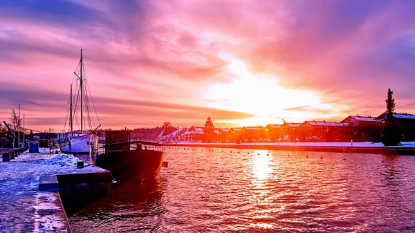 Scenico rosso viola e viola tramonto sul fiume campagna in Europa con vecchie navi che hanno riposo al molo del porto innevato — Foto Stock