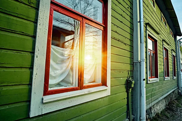 Fenster an der hölzernen grünen Wand des traditionellen alten ländlichen Landhauses in einem finnischen Dorf. Reflexion der Sonneneinstrahlung im Fenster — Stockfoto