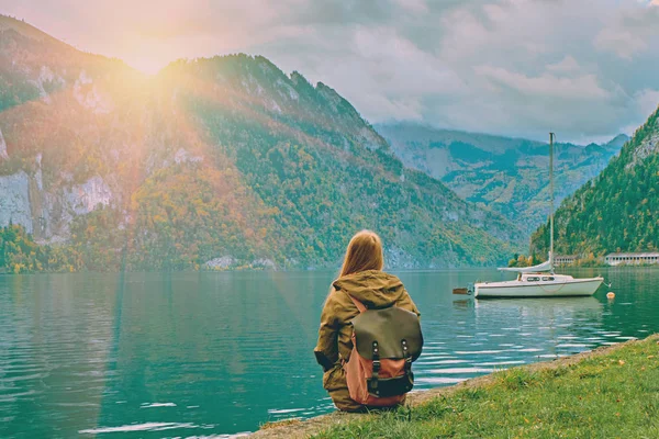 Genç turist kız güzel doğal doğarken Avusturya Alplerinde gölde seyir sırt çantası ile. Hipster seyahat tatil alps dağlar kavram. Sakin huzurlu alps göl kenarında güzel yat tekne. Tonda