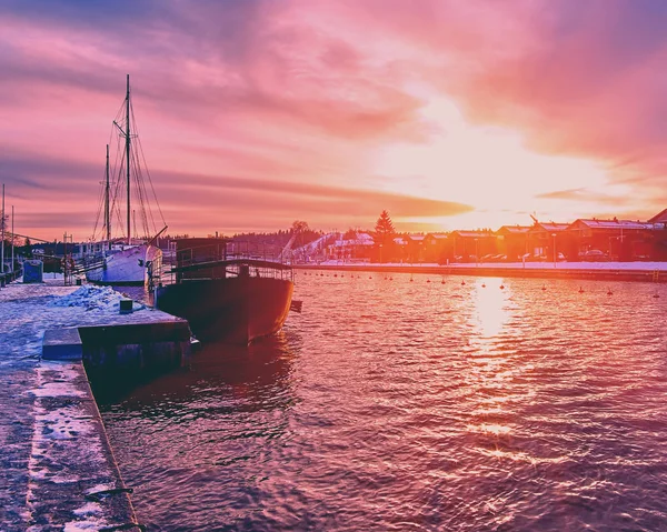 Escénica puesta de sol roja púrpura y violeta sobre el río del campo en Europa con viejos barcos descansando en el muelle del puerto nevado — Foto de Stock