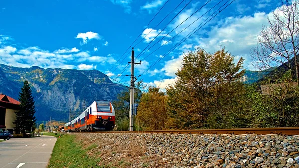 Roter blauer Zug in Bewegung in den österreichischen Alpen. Hochgeschwindigkeitszug erreicht Hallstatt obertraun Bahnhof in den Bergen. Lage: resort village hallstatt, salzkammergut, Österreich Stockfoto