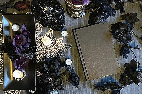 dark and gothic black aesthetic of blank book cover on wooden background with flowers.